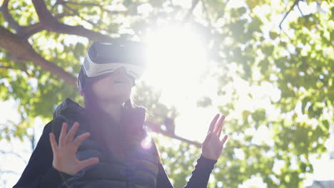 Amazed-young-dark-haired-woman-in-warm-black-waistcoat-wearing-virtual-reality-glasses-in-early-autumn-park